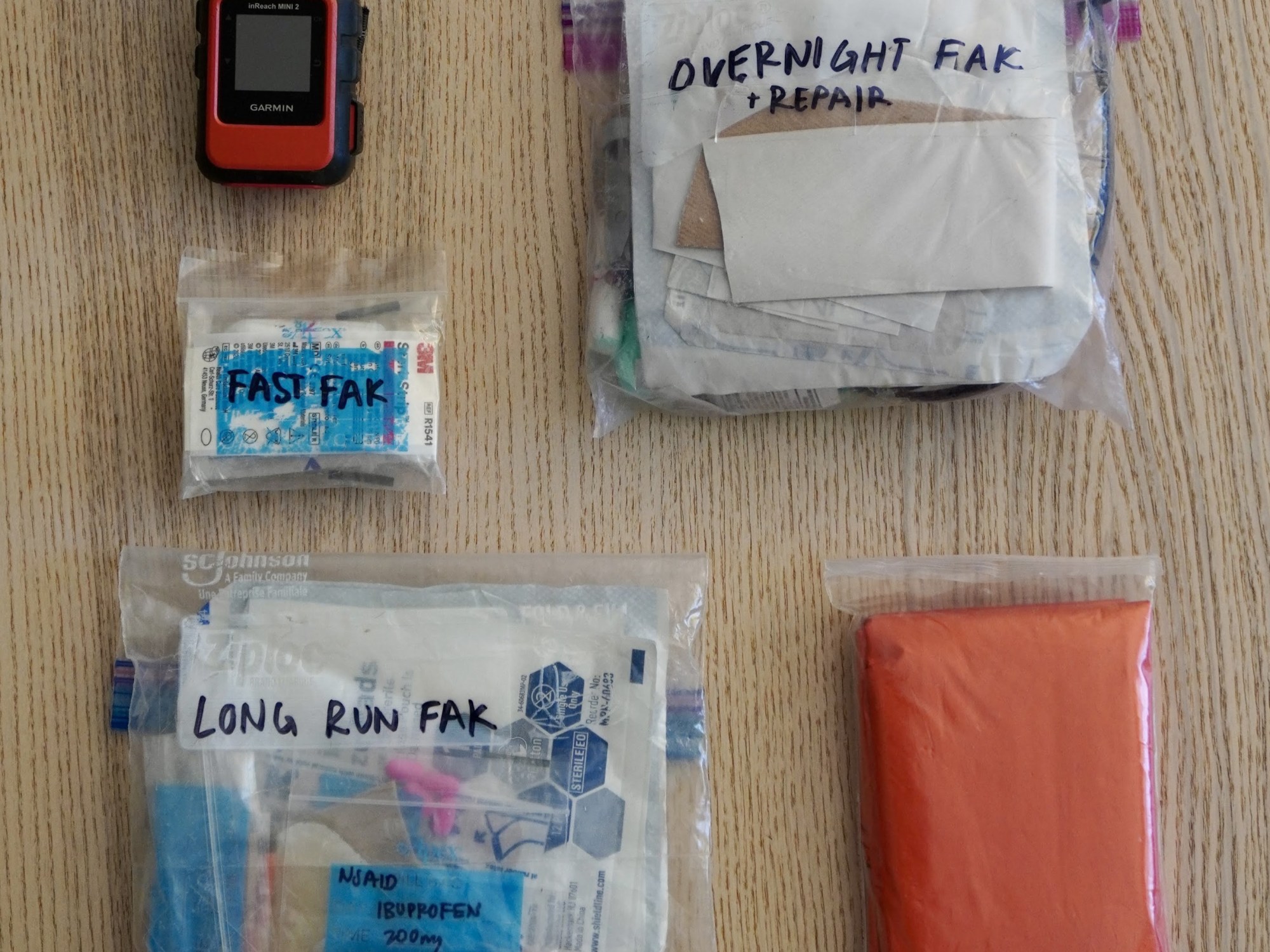 image of a garmin inreach satellite messenger, 3 first aid kits of different sizes, and an emergency blanket
