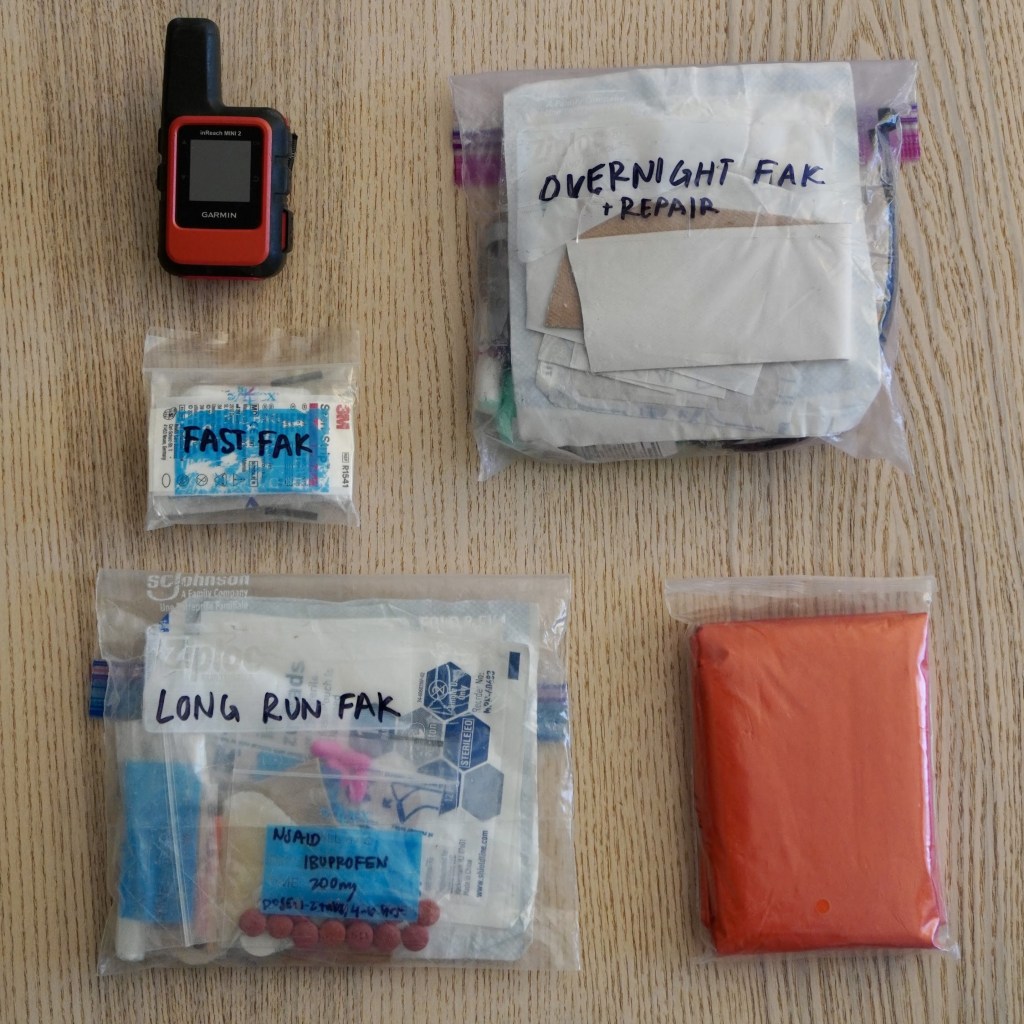image of a garmin inreach satellite messenger, 3 first aid kits of different sizes, and an emergency blanket